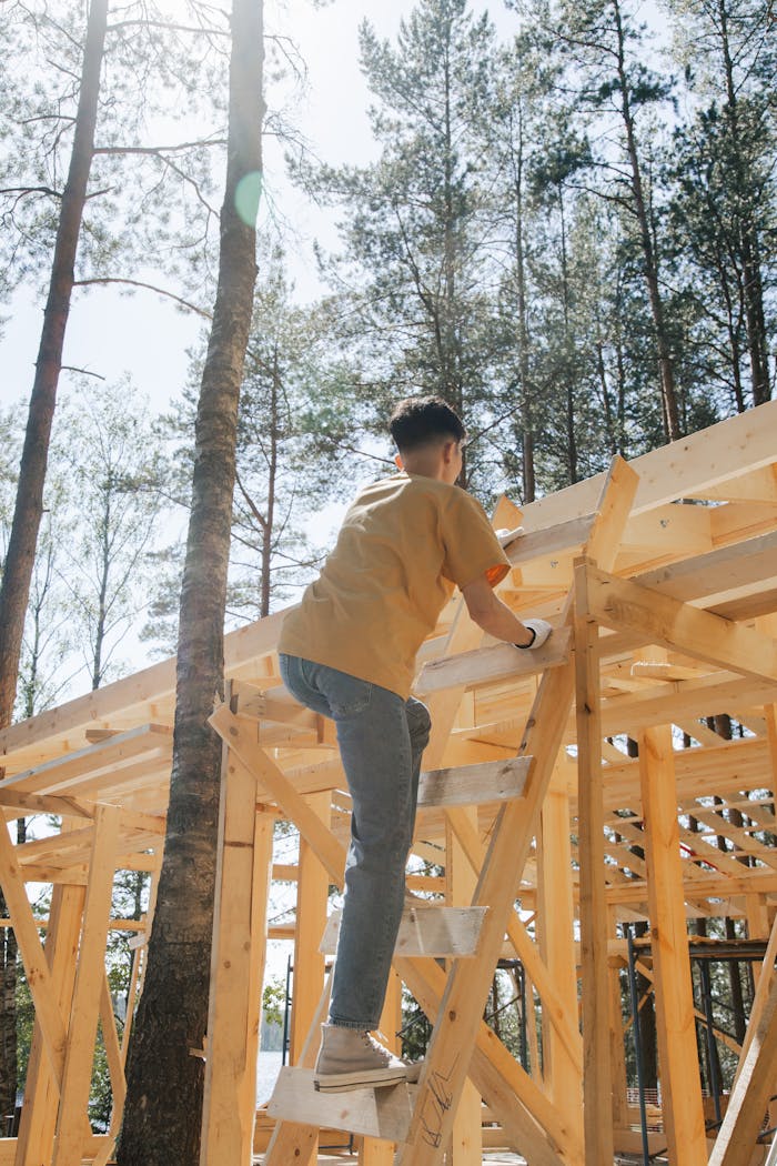 A worker in a yellow shirt climbs a wooden ladder on an outdoor construction site.